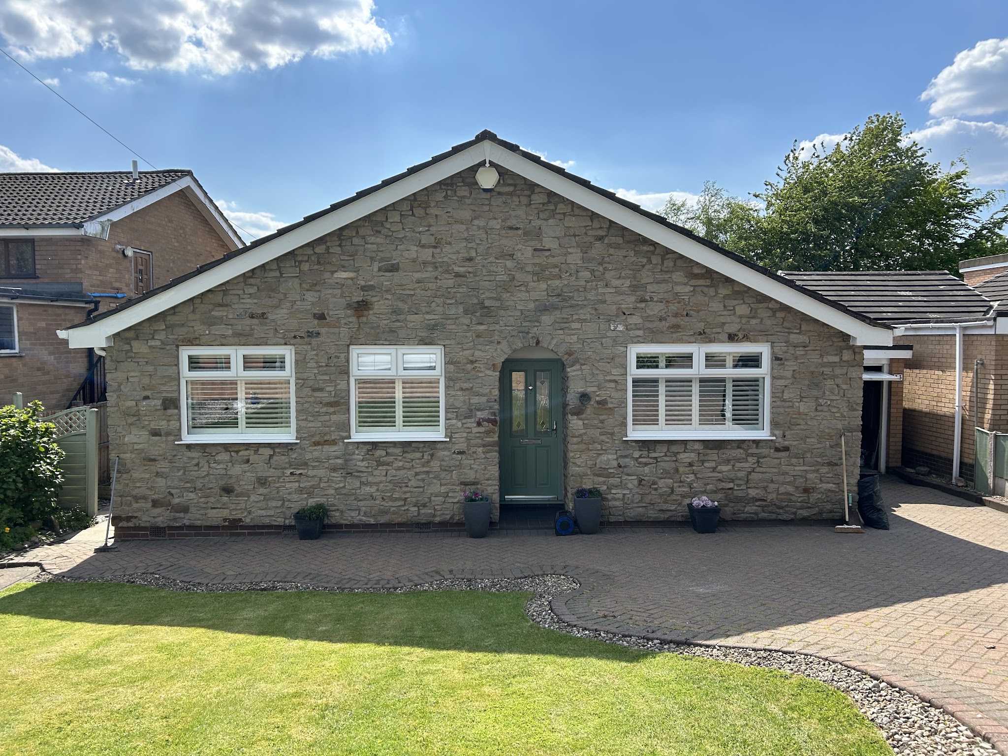 A stone bungalow with white windows and a green front door