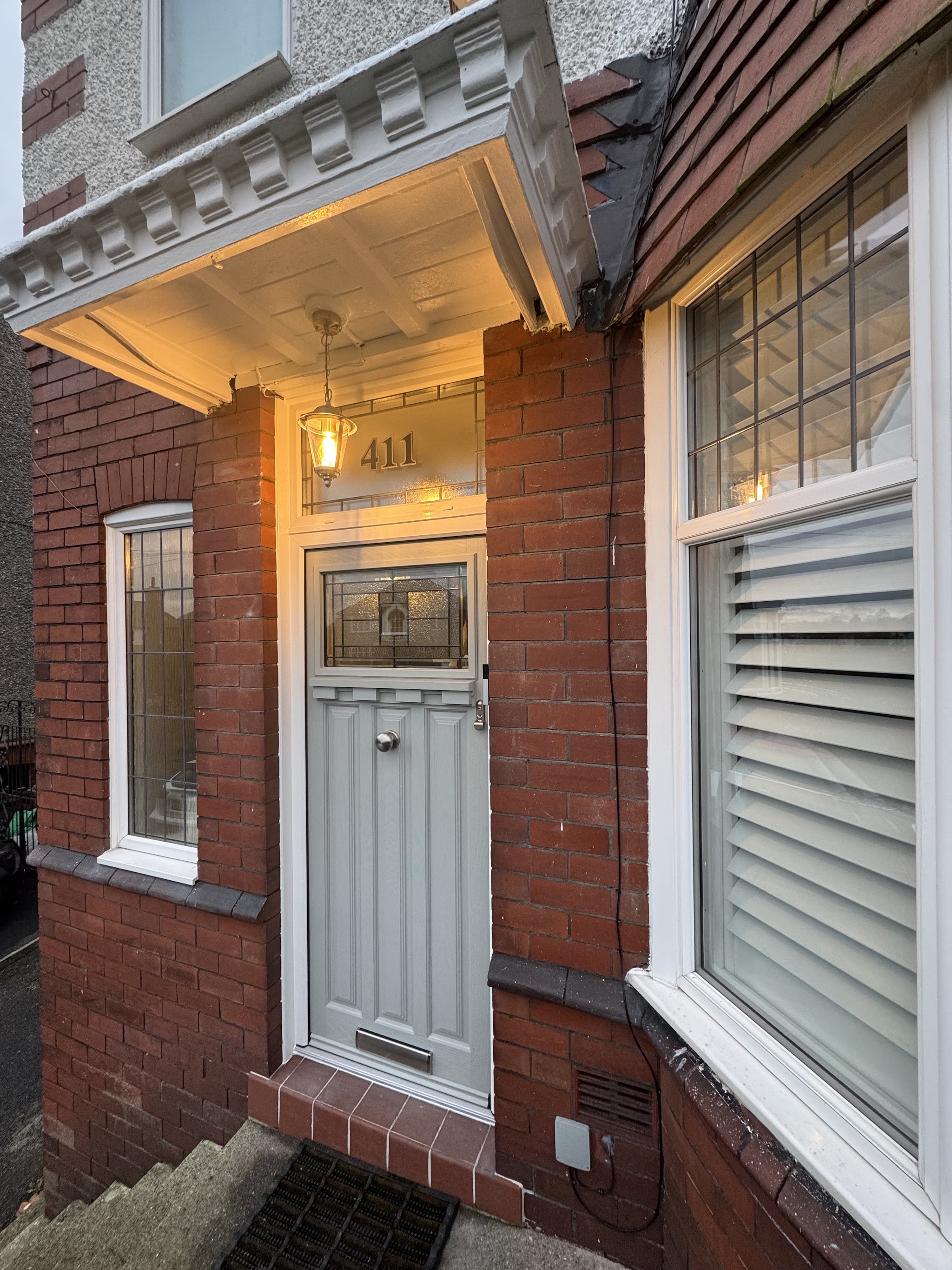A new sage-grey front door under a tiled porch, with new windows beside it
