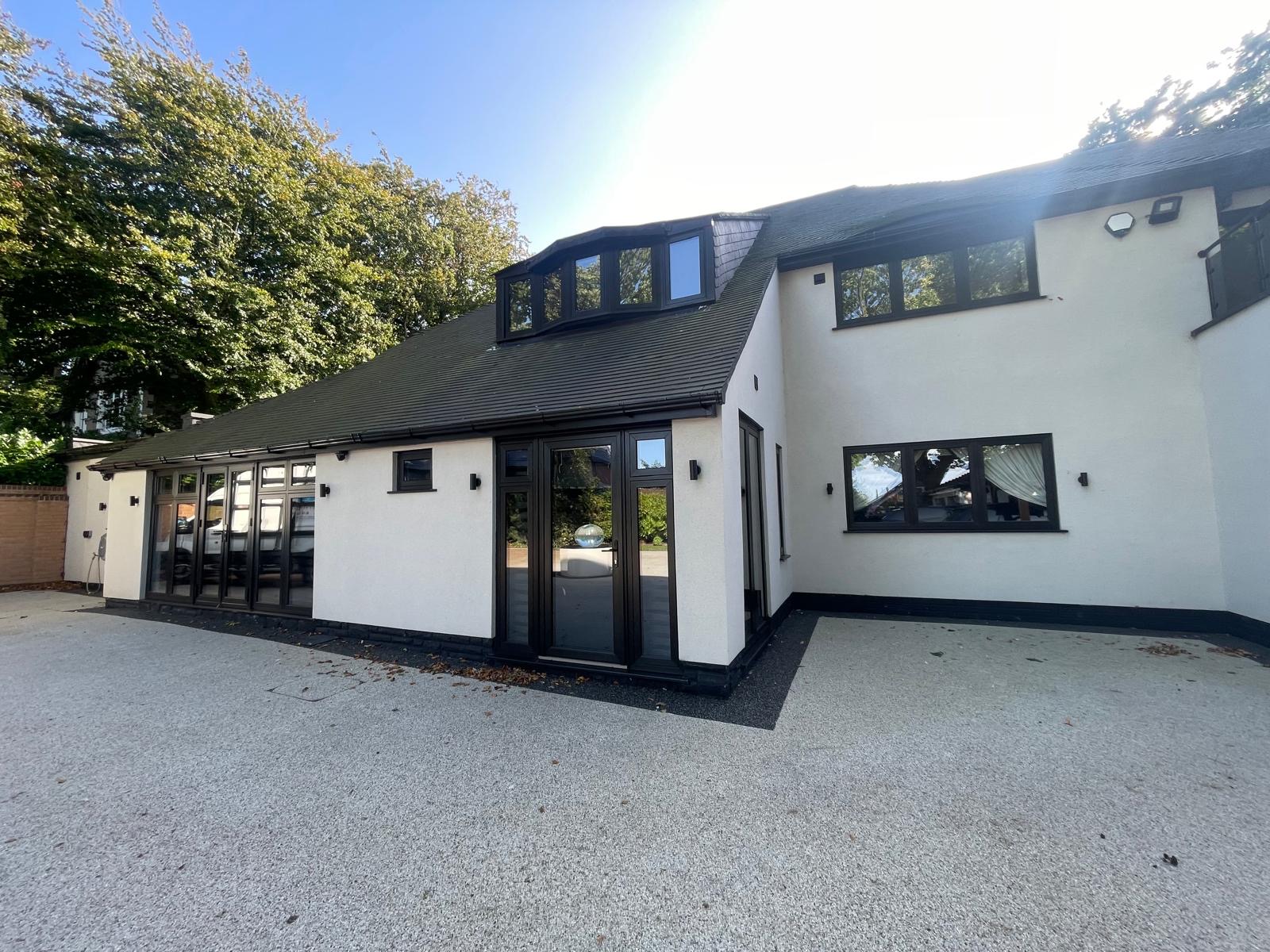 A white rendered house with black framed windows and wide glazed doors